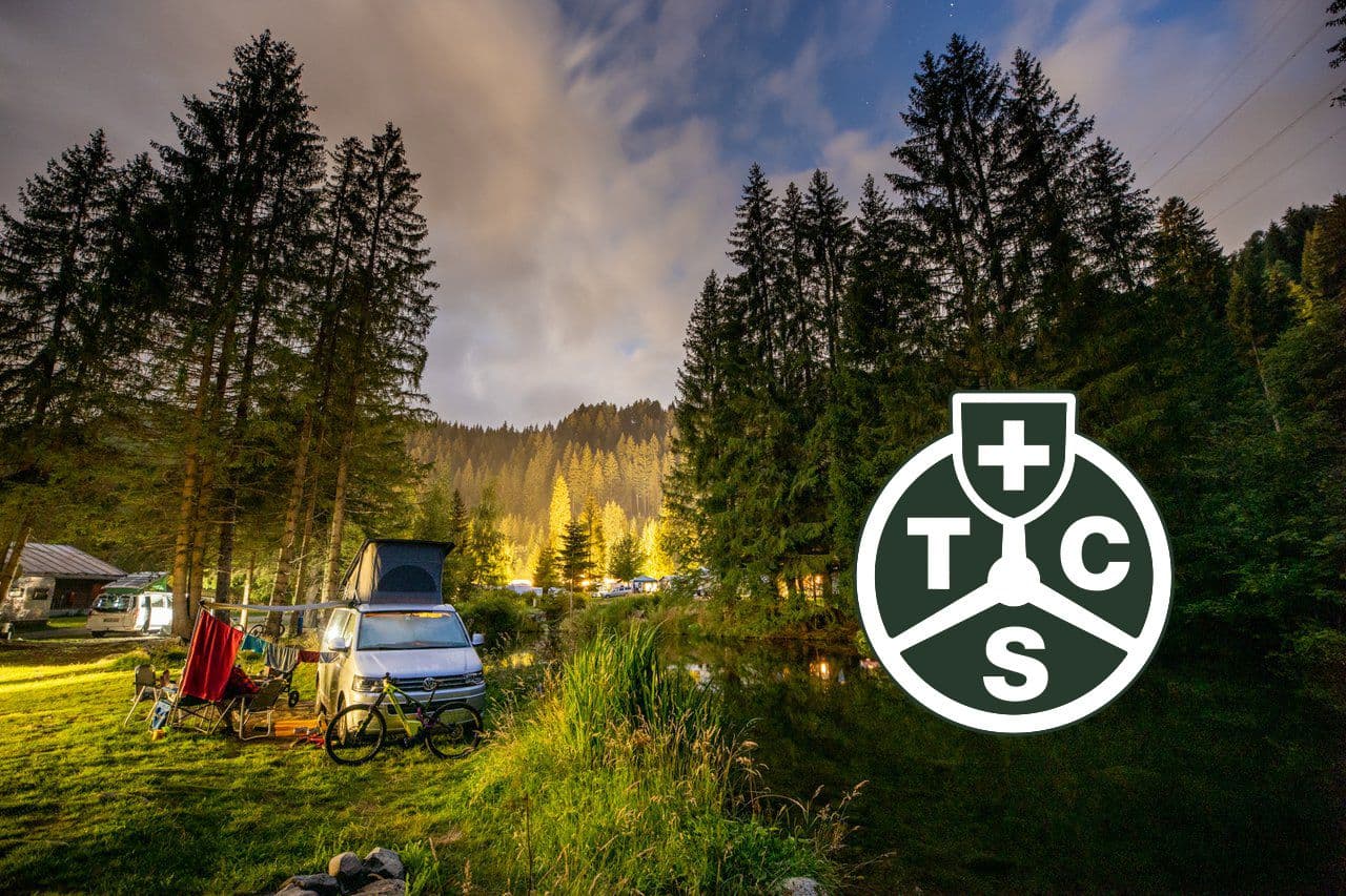 Campingplatz im Wald bei Dämmerung mit TCS-Logo